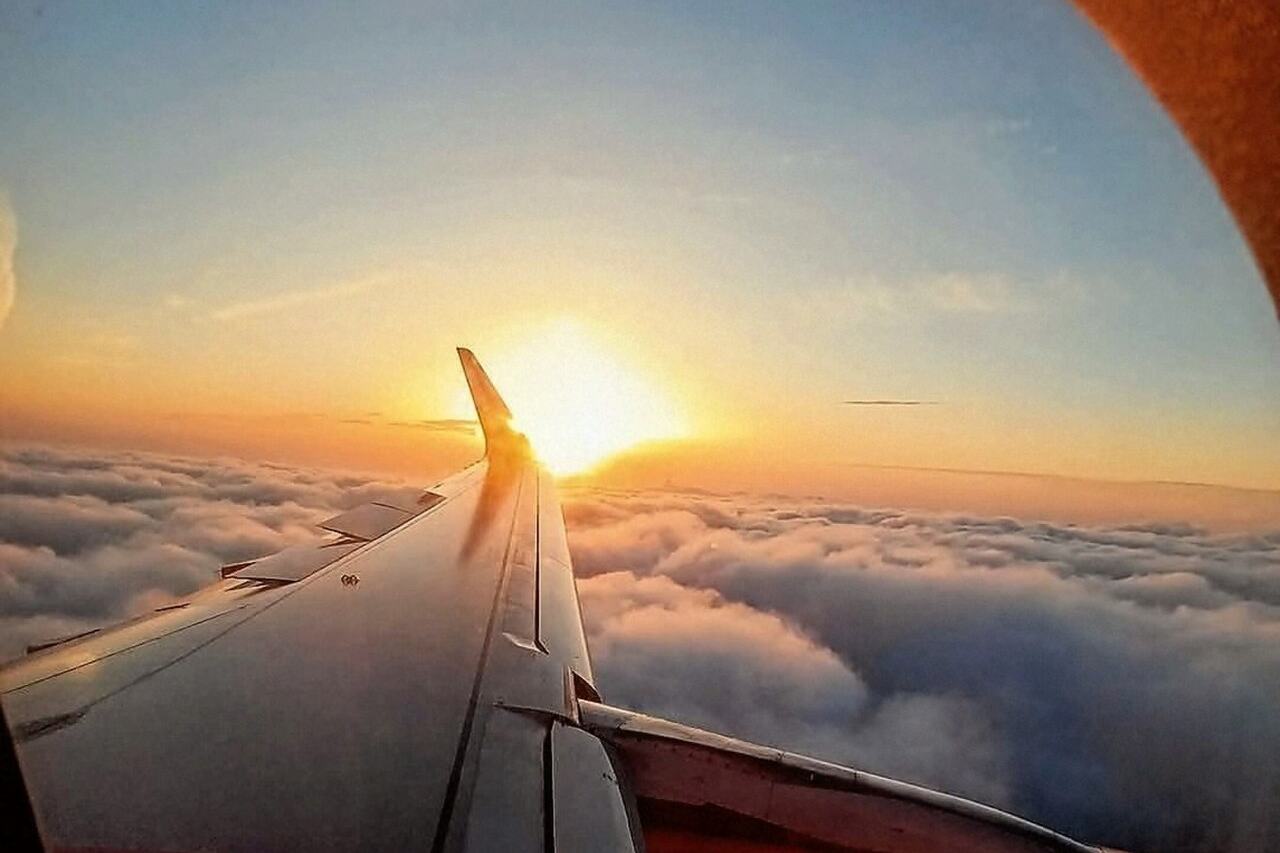El ala de un avión sobre las nubes al atardecer, vista desde la ventanilla